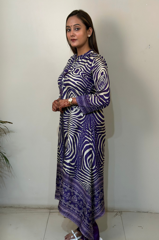 Woman wearing a long, patterned dress against a plain wall.