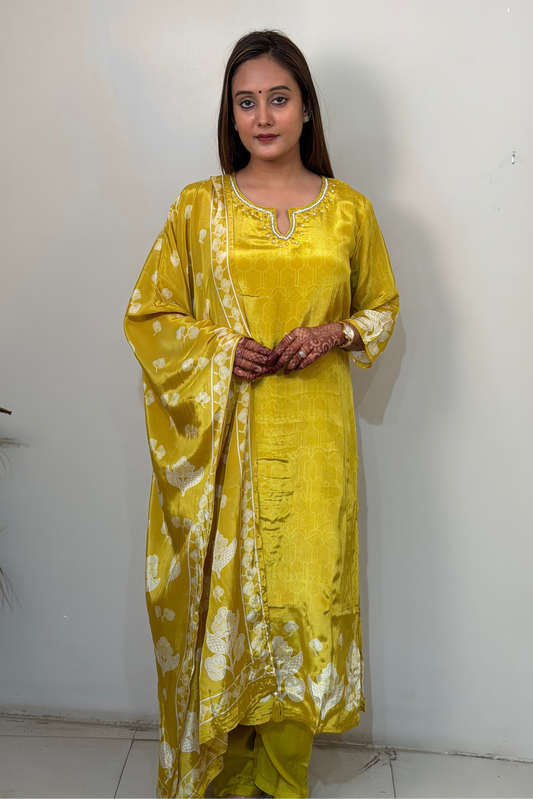 Woman wearing a yellow kurta with white patterns against a white wall.