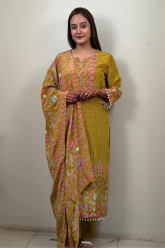 Woman wearing a yellow patterned saree standing against a plain wall.